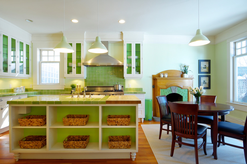 This is an example of a traditional eat-in kitchen in Calgary with stainless steel appliances, tile benchtops, a farmhouse sink, glass-front cabinets, white cabinets, green splashback and green benchtop.