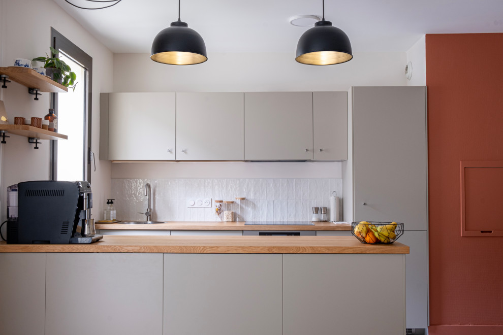 Photo of a medium sized contemporary galley open plan kitchen in Nantes with a single-bowl sink, beaded cabinets, beige cabinets, wood worktops, white splashback, ceramic splashback, stainless steel appliances, ceramic flooring, an island, grey floors and beige worktops.
