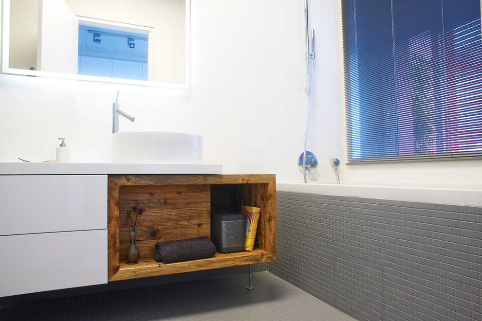 Geräumiges Industrial Badezimmer En Suite mit flächenbündigen Schrankfronten, weißen Schränken, Einbaubadewanne, bodengleicher Dusche, Wandtoilette mit Spülkasten, grauen Fliesen, Mosaikfliesen, weißer Wandfarbe, Keramikboden, Aufsatzwaschbecken, Mineralwerkstoff-Waschtisch, grauem Boden, offener Dusche und weißer Waschtischplatte in Berlin