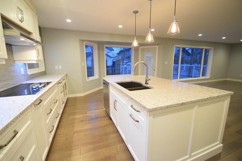 Inspiration for a transitional l-shaped vinyl floor eat-in kitchen remodel in Edmonton with a double-bowl sink, shaker cabinets, white cabinets, quartz countertops, gray backsplash, glass tile backsplash, stainless steel appliances and an island