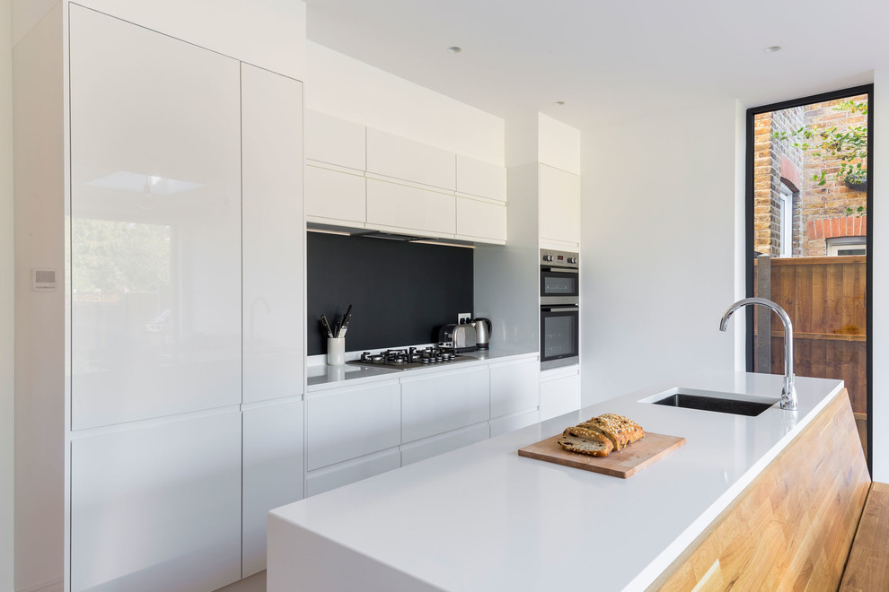 Inspiration for a large modern galley open plan kitchen in London with an integrated sink, flat-panel cabinets, white cabinets, quartzite benchtops, panelled appliances, with island and black splashback.