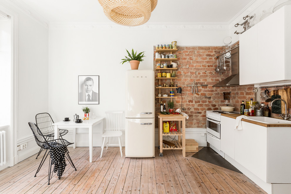 This is an example of a small scandinavian single-wall eat-in kitchen in Stockholm with a drop-in sink, flat-panel cabinets, white cabinets, wood benchtops, white appliances, light hardwood floors and with island.
