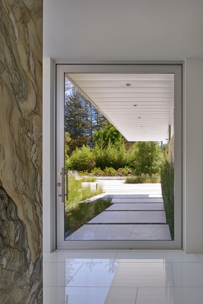 На фото: большая входная дверь в современном стиле с белыми стенами, бетонным полом, поворотной входной дверью, стеклянной входной дверью и белым полом с