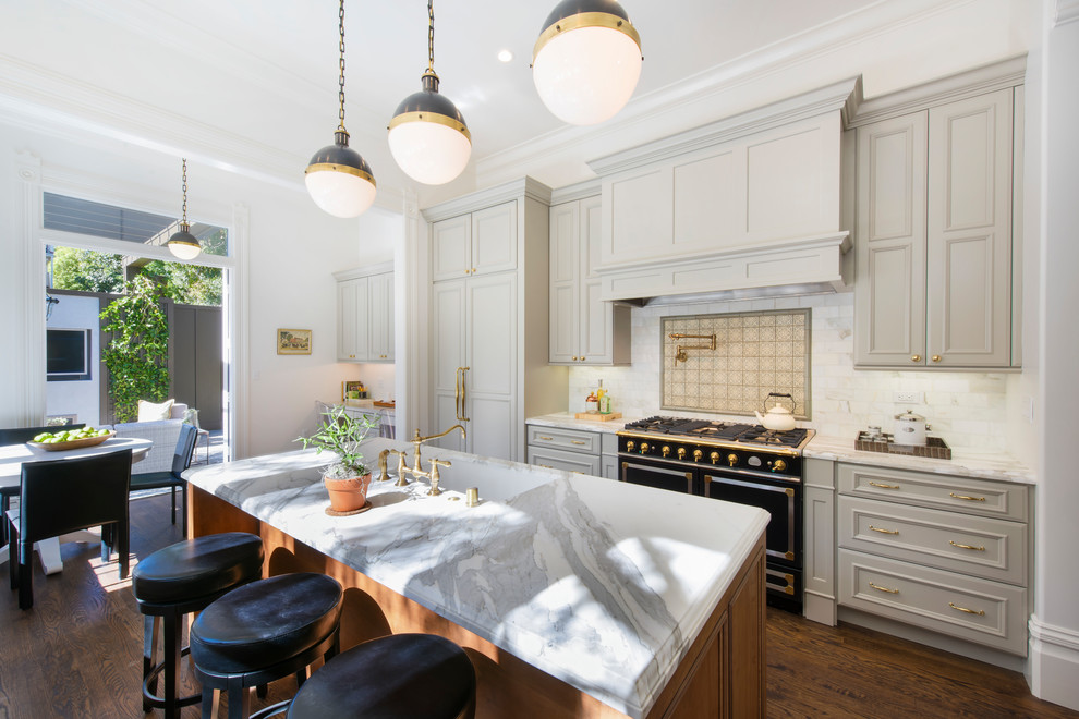 Photo of a mid-sized traditional galley eat-in kitchen in San Francisco with an undermount sink, flat-panel cabinets, grey cabinets, quartzite benchtops, white splashback, subway tile splashback, black appliances, medium hardwood floors, with island, brown floor and white benchtop.