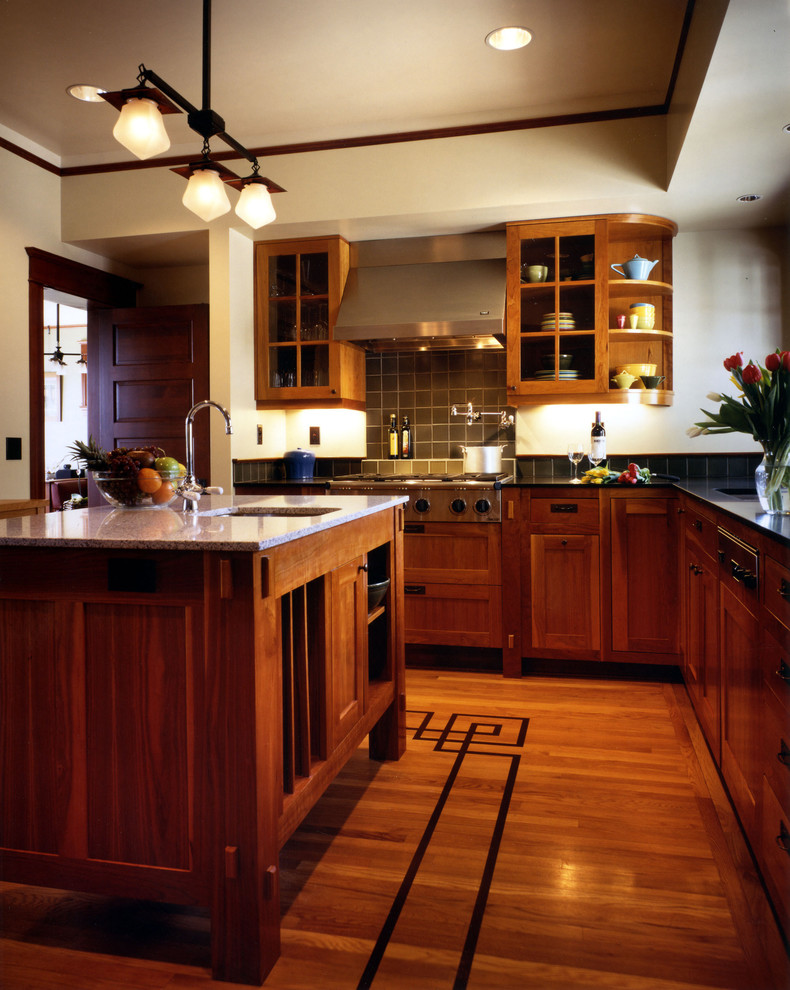 This is an example of an arts and crafts kitchen in Seattle with glass-front cabinets, stainless steel appliances, medium wood cabinets and green splashback.