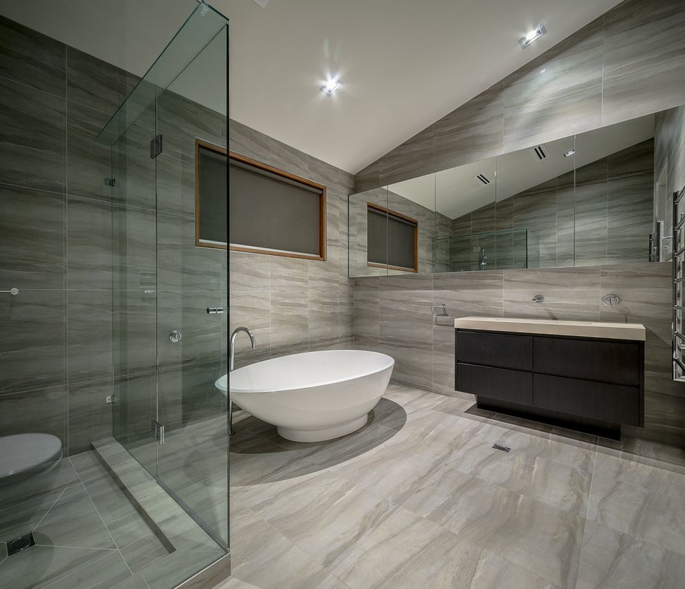 Photo of a mid-sized contemporary master bathroom in Melbourne with a freestanding tub, a corner shower, a one-piece toilet, porcelain tile, porcelain floors, a drop-in sink, flat-panel cabinets, dark wood cabinets and a hinged shower door.