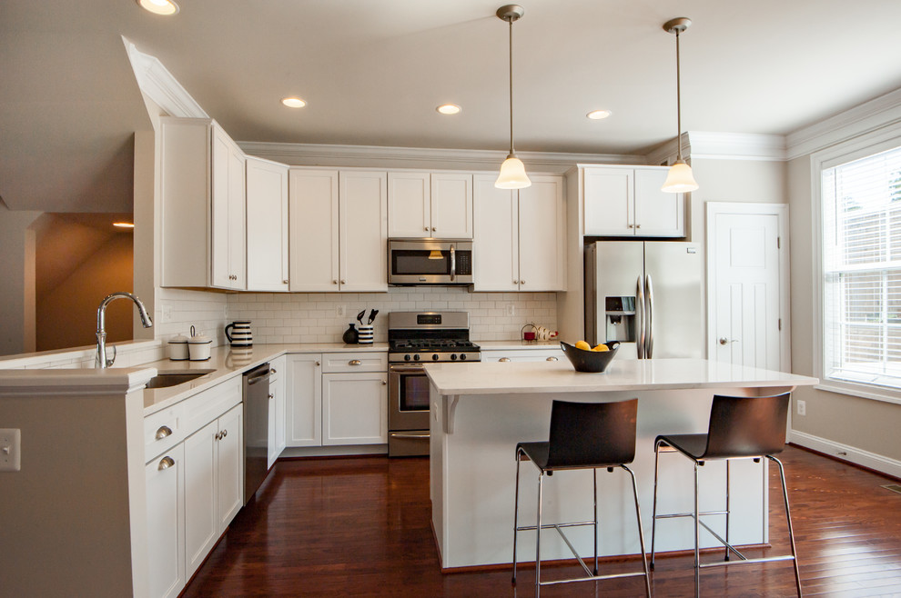 Inspiration for a transitional u-shaped dark wood floor and brown floor kitchen remodel with an undermount sink, shaker cabinets, white cabinets, white backsplash, subway tile backsplash, stainless steel appliances and an island