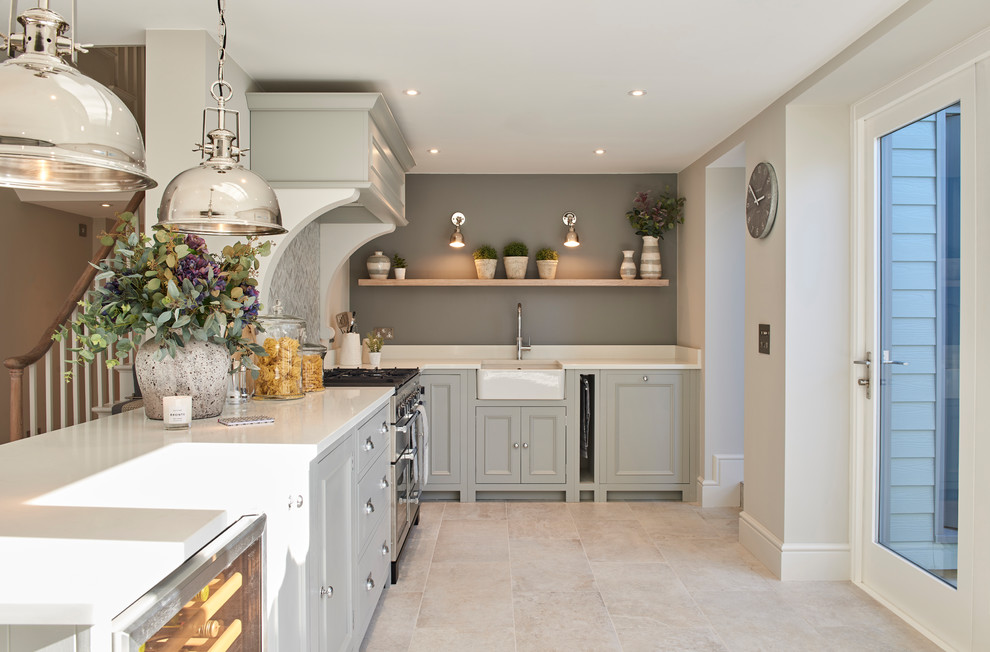 This is an example of a transitional l-shaped kitchen in Hertfordshire with a farmhouse sink, recessed-panel cabinets, grey cabinets, grey splashback, stainless steel appliances, beige floor and white benchtop.
