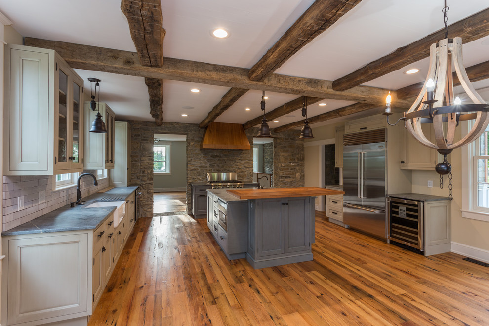 Design ideas for a country kitchen in DC Metro with a farmhouse sink, recessed-panel cabinets, soapstone benchtops, white splashback, brick splashback, stainless steel appliances, medium hardwood floors and with island.
