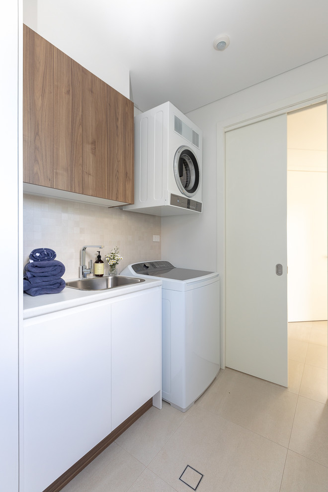 Inspiration for a beach style single-wall dedicated laundry room in Other with a drop-in sink, flat-panel cabinets, white cabinets, white walls, beige floor and white benchtop.