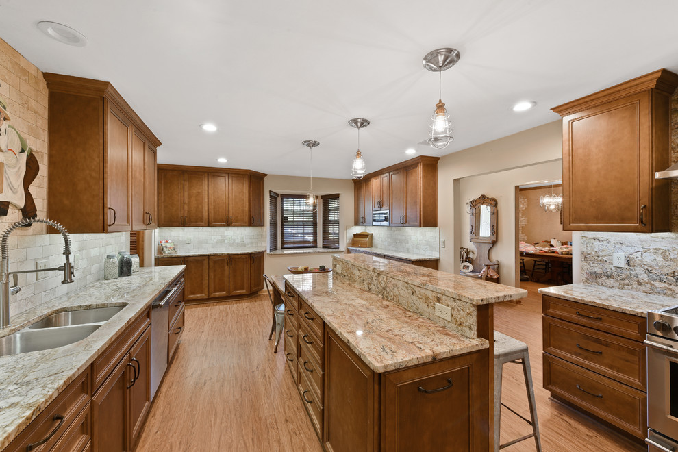 Expansive contemporary galley separate kitchen in Jacksonville with a double-bowl sink, raised-panel cabinets, medium wood cabinets, granite benchtops, grey splashback, travertine splashback, stainless steel appliances, vinyl floors, with island and brown floor.