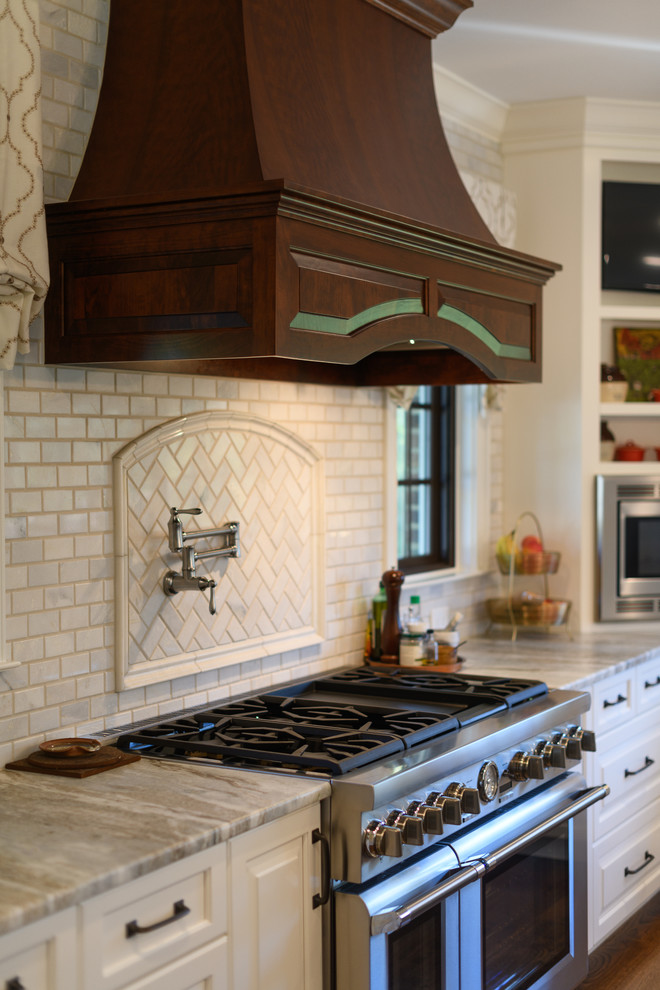 Example of a large transitional l-shaped dark wood floor and brown floor kitchen design with an undermount sink, raised-panel cabinets, white cabinets, quartzite countertops, white backsplash, marble backsplash, stainless steel appliances and an island