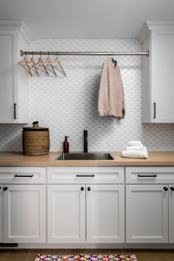 Inspiration for a large scandinavian single-wall dedicated laundry room in Detroit with a drop-in sink, shaker cabinets, white cabinets, wood benchtops, white splashback, ceramic splashback, blue walls, light hardwood floors, a side-by-side washer and dryer and brown benchtop.