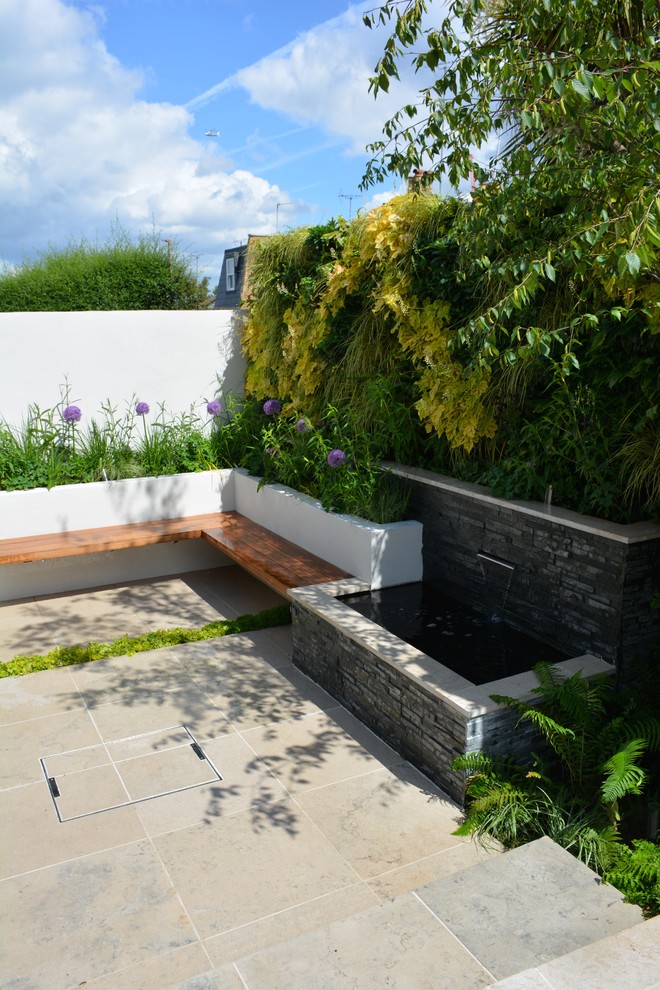 This is an example of a contemporary garden in London with a vertical garden and natural stone pavers.
