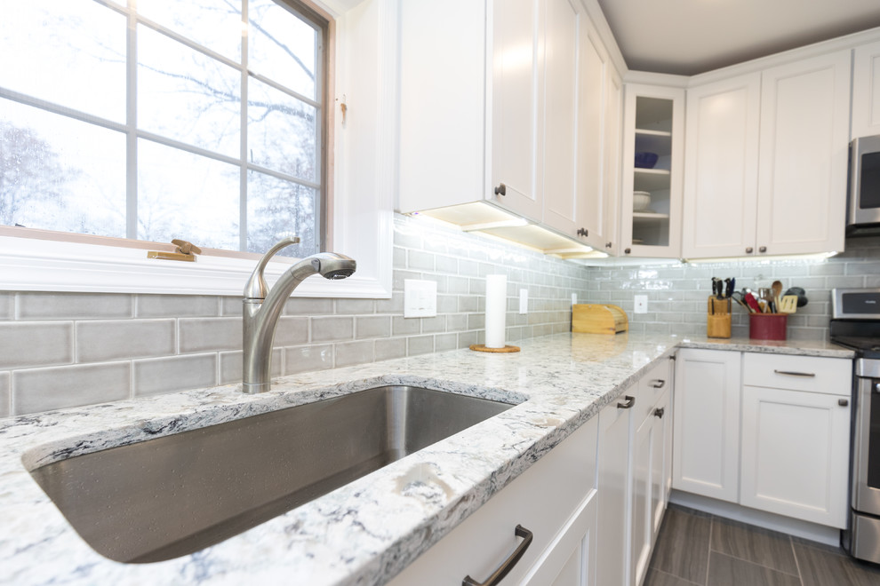 Mid-sized transitional l-shaped porcelain tile and brown floor enclosed kitchen photo in San Diego with an undermount sink, beaded inset cabinets, white cabinets, granite countertops, gray backsplash, ceramic backsplash, stainless steel appliances, no island and gray countertops