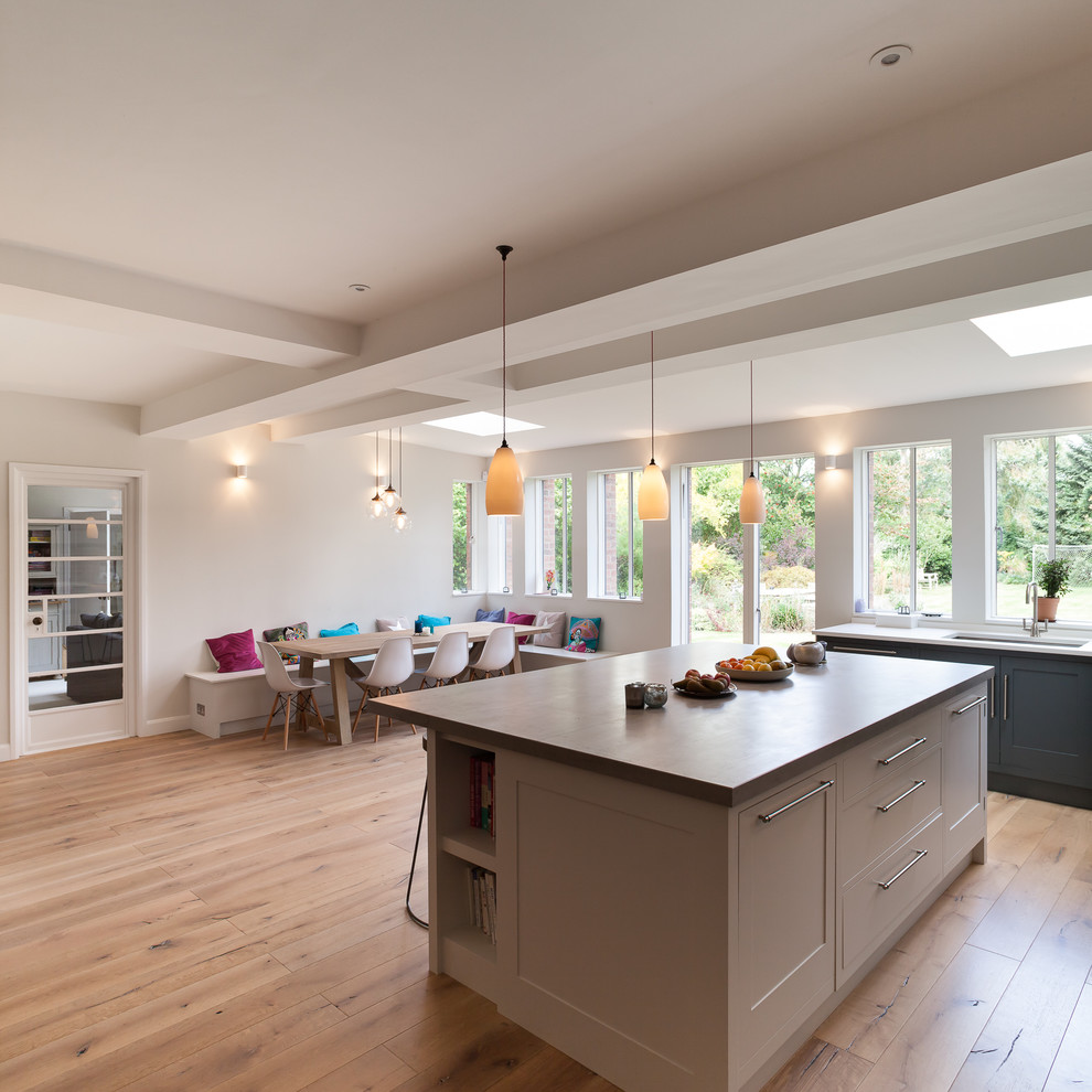Design ideas for a large contemporary l-shaped kitchen/diner in London with a built-in sink, flat-panel cabinets, grey cabinets, concrete worktops, integrated appliances, medium hardwood flooring and a breakfast bar.