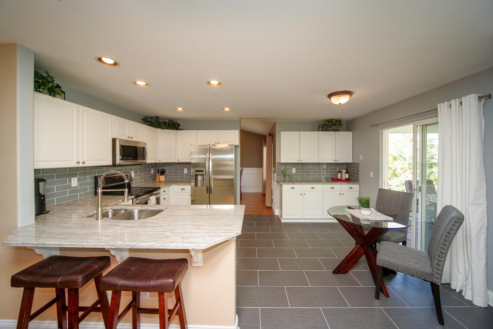 Large country u-shaped eat-in kitchen in Denver with a double-bowl sink, raised-panel cabinets, white cabinets, granite benchtops, subway tile splashback, stainless steel appliances, grey splashback, porcelain floors, a peninsula and grey floor.