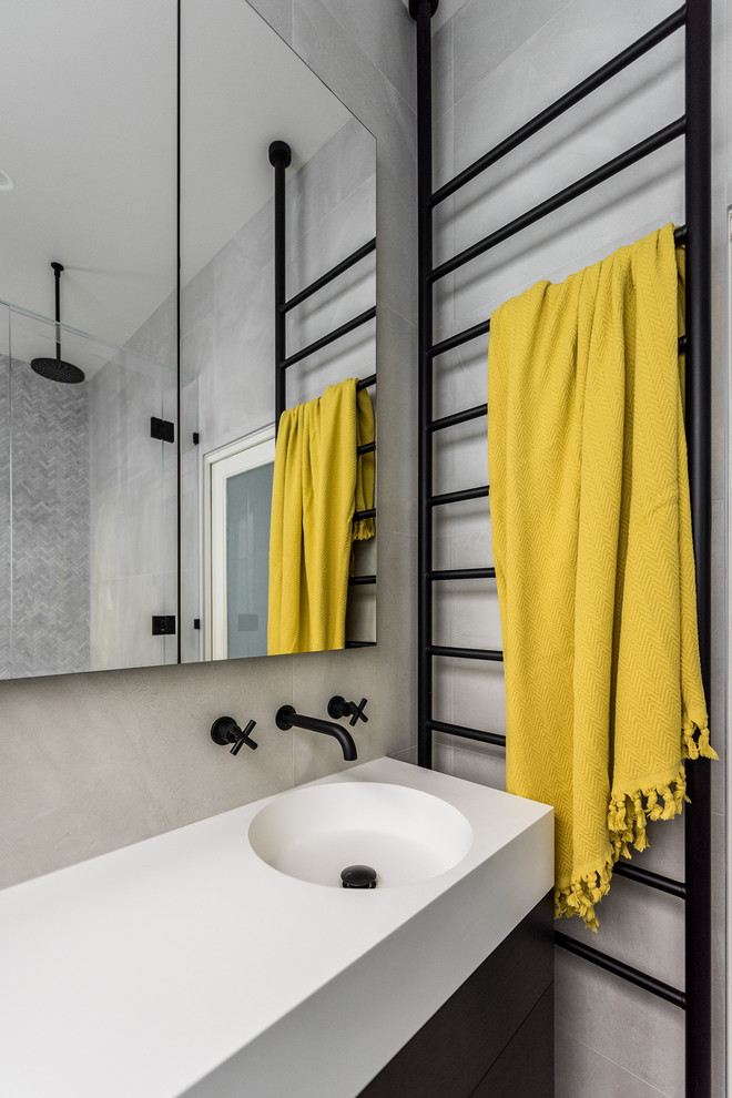 This is an example of a mid-sized contemporary master wet room bathroom in Melbourne with flat-panel cabinets, dark wood cabinets, a drop-in tub, a one-piece toilet, gray tile, porcelain tile, grey walls, porcelain floors, an integrated sink, solid surface benchtops, grey floor and a hinged shower door.