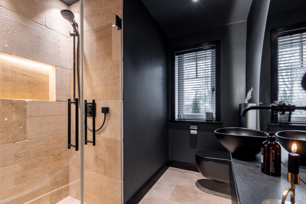 Inredning av ett modernt litet svart svart badrum med dusch, med släta luckor, svarta skåp, en kantlös dusch, en toalettstol med hel cisternkåpa, svart kakel, svarta väggar, travertin golv, ett fristående handfat, bänkskiva i akrylsten, beiget golv och dusch med gångjärnsdörr
