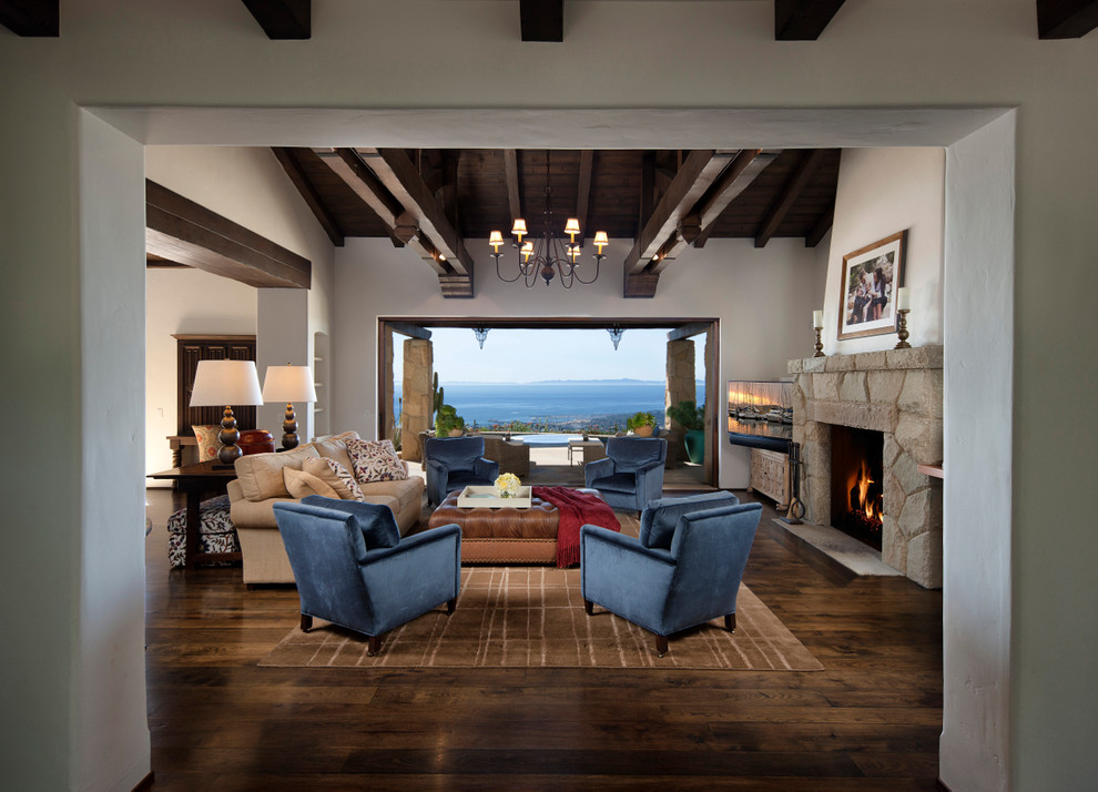 This is an example of a mediterranean family room in Santa Barbara with white walls, dark hardwood floors, a standard fireplace and a stone fireplace surround.