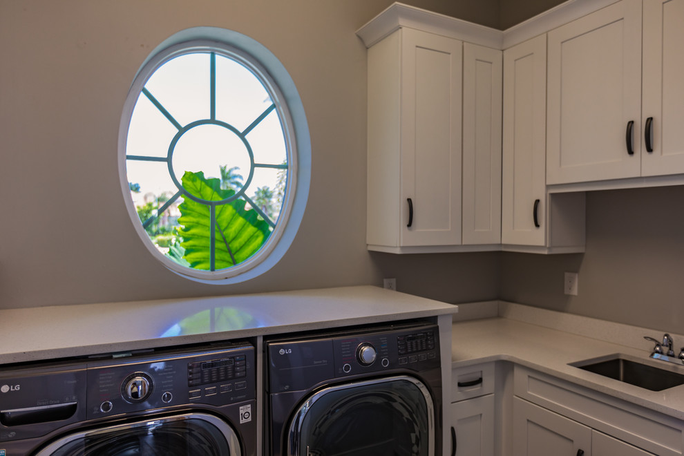 Mid-sized transitional l-shaped dedicated laundry room in Miami with an undermount sink, shaker cabinets, white cabinets, limestone benchtops, white walls and a side-by-side washer and dryer.