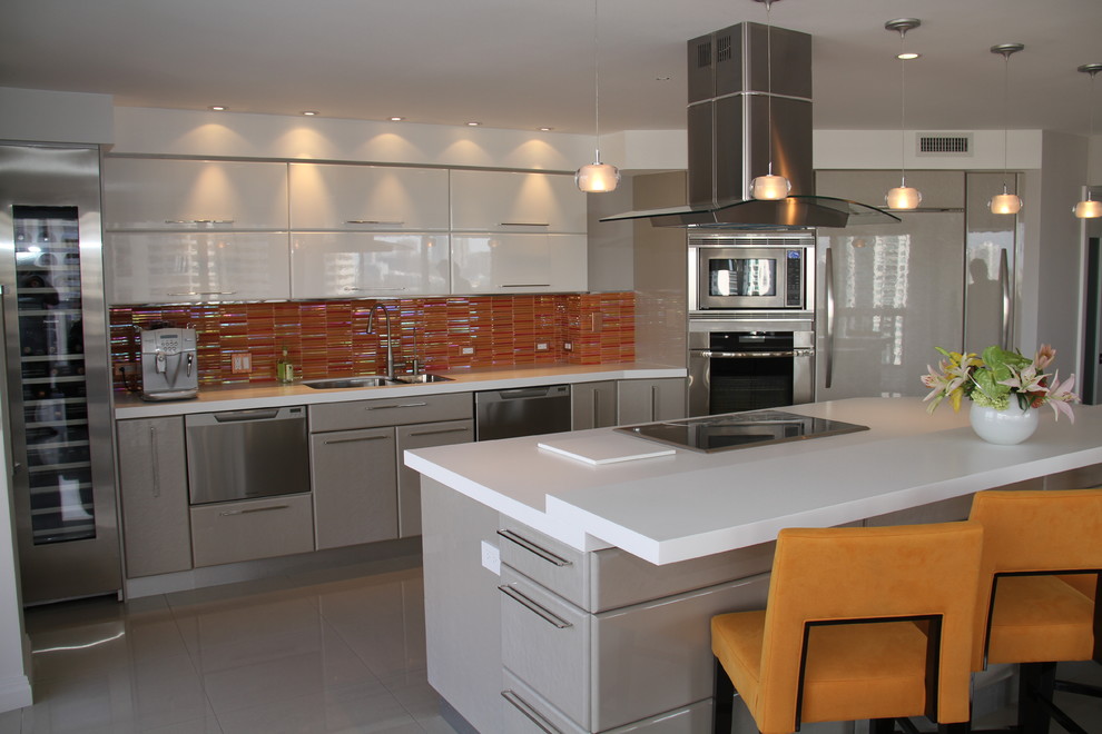This is an example of a large contemporary single-wall kitchen in Miami with with island, flat-panel cabinets, grey cabinets, solid surface benchtops, orange splashback, an undermount sink, stainless steel appliances and glass tile splashback.
