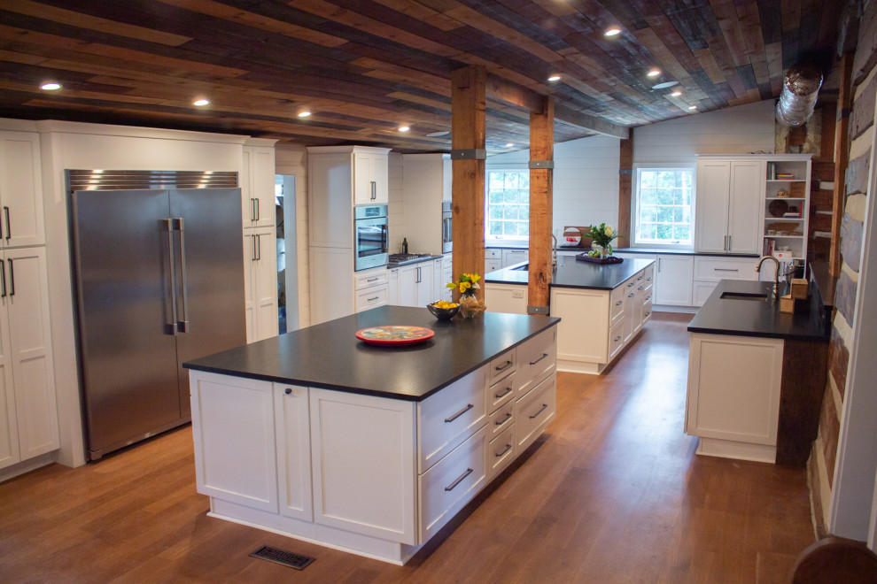 Photo of a large traditional kitchen/diner in Nashville with a submerged sink, shaker cabinets, white cabinets, engineered stone countertops, white splashback, tonge and groove splashback, stainless steel appliances, medium hardwood flooring, multiple islands, brown floors, black worktops and a wood ceiling.