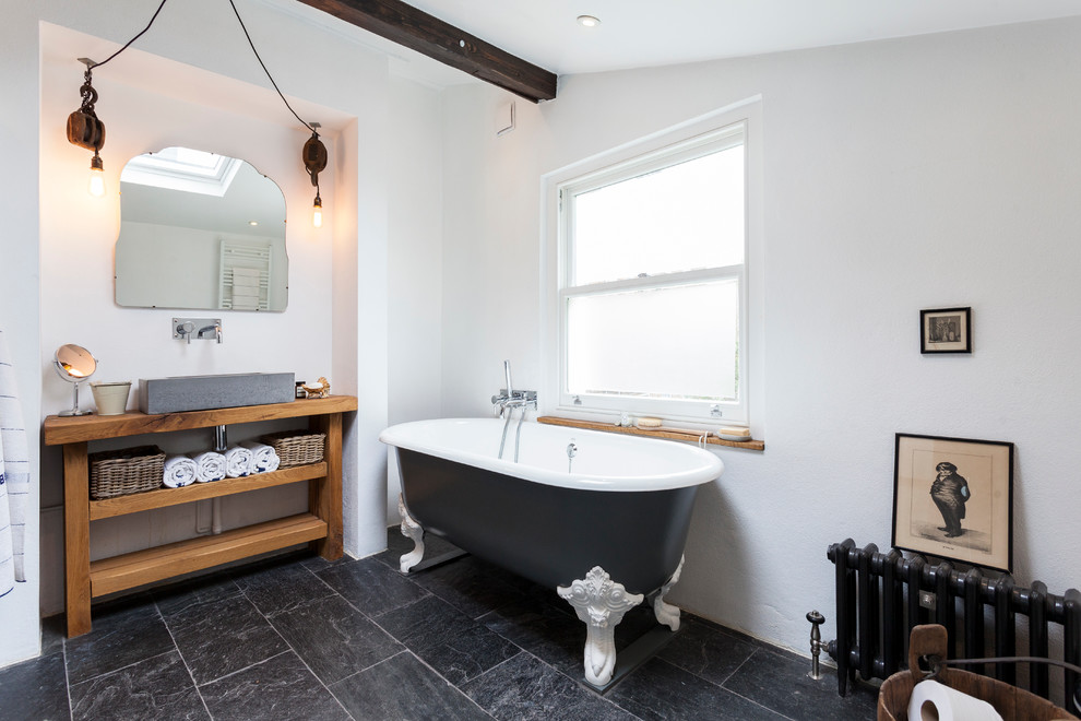 Scandinavian bathroom in London with a vessel sink, open cabinets, medium wood cabinets, wood benchtops, a claw-foot tub, white tile, white walls and slate floors.