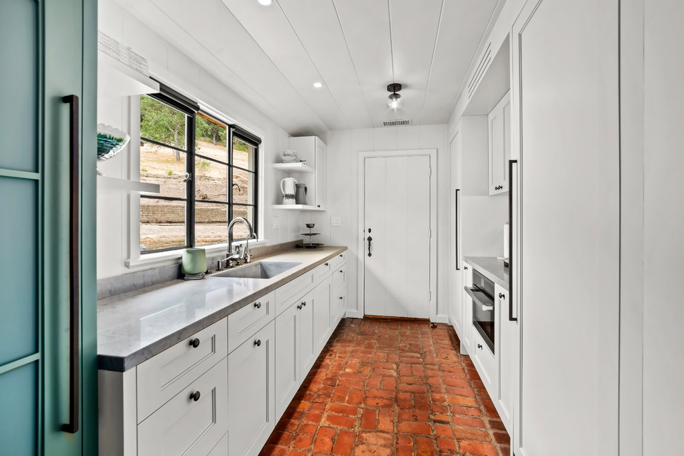 This is an example of a mid-sized arts and crafts single-wall kitchen pantry in Other with an undermount sink, white cabinets, stainless steel appliances, brick floors, recessed-panel cabinets and grey benchtop.