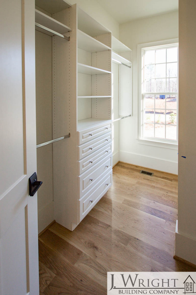 Photo of a large country gender-neutral walk-in wardrobe in Birmingham with open cabinets, white cabinets, light hardwood floors and brown floor.