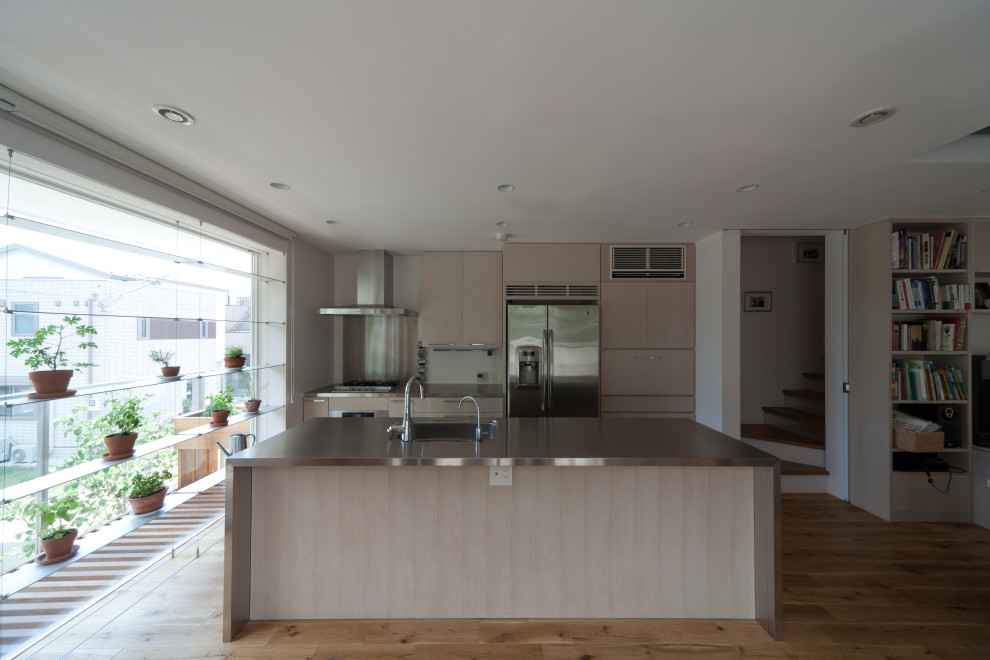 This is an example of a large modern galley open plan kitchen in Tokyo with an integrated sink, flat-panel cabinets, light wood cabinets, stainless steel benchtops, grey splashback, ceramic splashback, plywood floors, with island, beige floor, grey benchtop and timber.