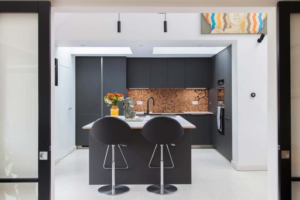 Large contemporary grey and black l-shaped open plan kitchen in London with black cabinets, wood worktops, integrated appliances, cork flooring, an island, white floors, white worktops and a vaulted ceiling.