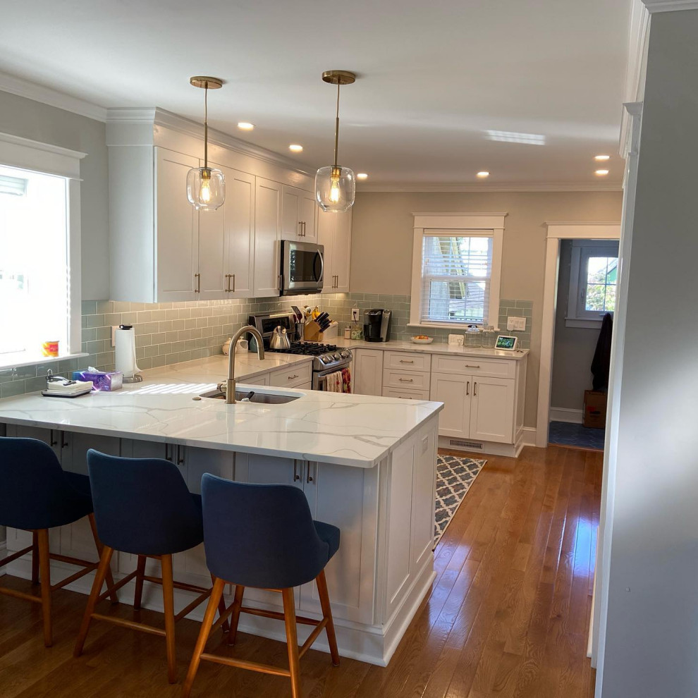 Photo of a mid-sized transitional l-shaped eat-in kitchen in Other with an undermount sink, shaker cabinets, white cabinets, quartz benchtops, grey splashback, glass tile splashback, stainless steel appliances, medium hardwood floors, no island, brown floor and white benchtop.