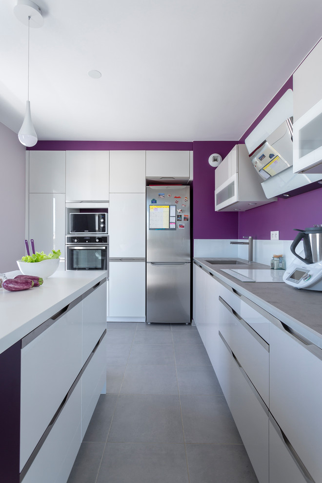 This is an example of a mid-sized contemporary l-shaped kitchen in Paris with an undermount sink, white cabinets, white splashback, stainless steel appliances, with island, grey floor, flat-panel cabinets and white benchtop.