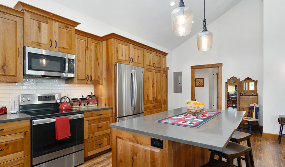 Inspiration for a large rustic medium tone wood floor, brown floor and vaulted ceiling kitchen remodel with a farmhouse sink, raised-panel cabinets, medium tone wood cabinets, concrete countertops, white backsplash, ceramic backsplash, stainless steel appliances, an island and gray countertops