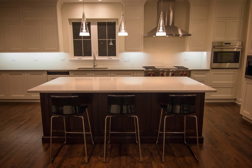 Mid-sized transitional l-shaped dark wood floor enclosed kitchen photo in Chicago with an undermount sink, recessed-panel cabinets, white cabinets, solid surface countertops, white backsplash, porcelain backsplash, stainless steel appliances and an island