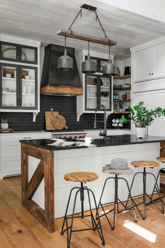 Inspiration for a mid-sized l-shaped open plan kitchen in Atlanta with a farmhouse sink, shaker cabinets, white cabinets, quartz benchtops, black splashback, ceramic splashback, panelled appliances, medium hardwood floors, with island, brown floor, black benchtop and wood.