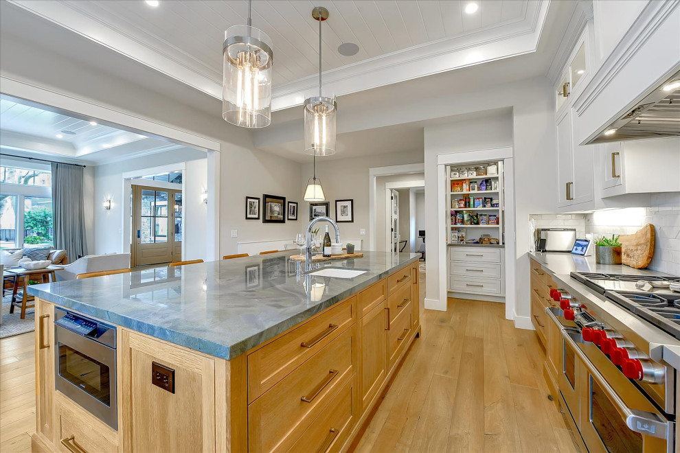 Example of a large arts and crafts l-shaped medium tone wood floor, brown floor and tray ceiling open concept kitchen design in San Francisco with shaker cabinets, medium tone wood cabinets, white backsplash, subway tile backsplash, stainless steel appliances, an island, gray countertops and an undermount sink