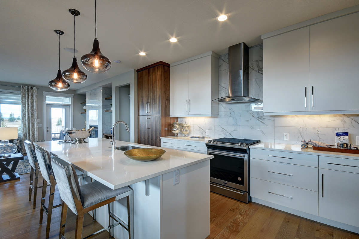 Inspiration for a mid-sized transitional single-wall light wood floor and beige floor enclosed kitchen remodel in Calgary with an undermount sink, flat-panel cabinets, white cabinets, quartz countertops, white backsplash, stainless steel appliances and an island