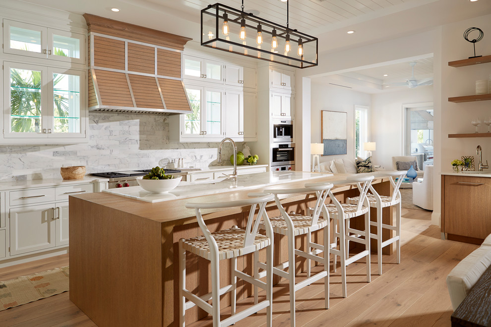 Photo of a beach style galley eat-in kitchen in Miami with shaker cabinets, white cabinets, wood benchtops, grey splashback, stainless steel appliances, medium hardwood floors, with island and brown floor.