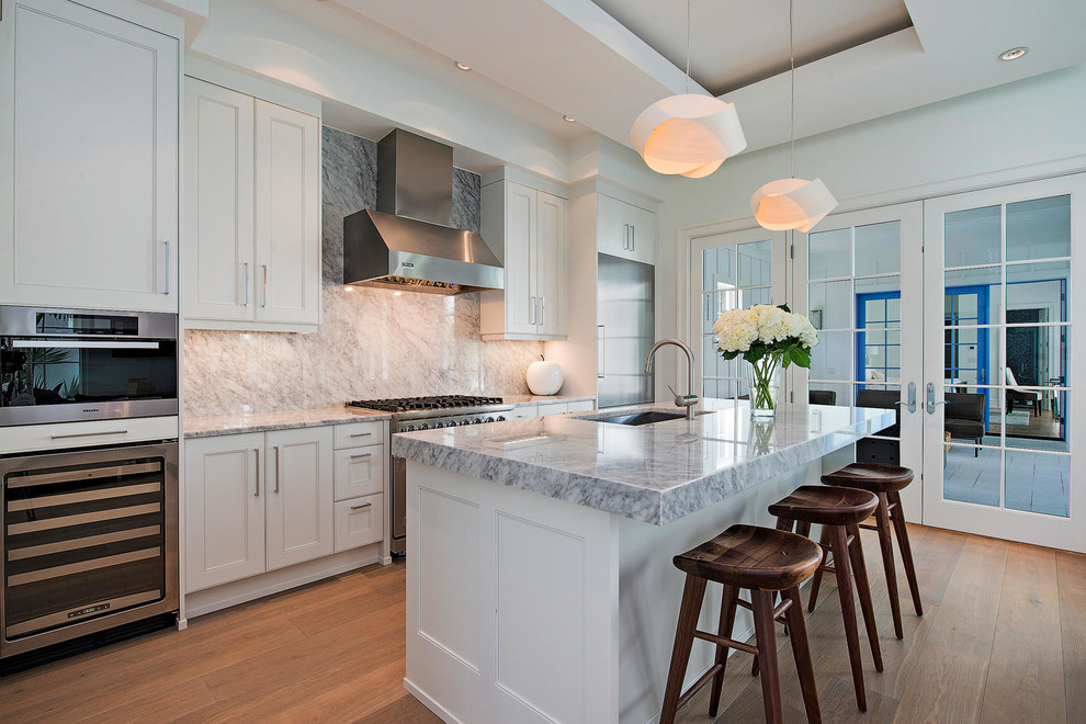 Mid-sized transitional u-shaped medium tone wood floor open concept kitchen photo in Miami with an undermount sink, shaker cabinets, white cabinets, marble countertops, gray backsplash, stainless steel appliances and an island