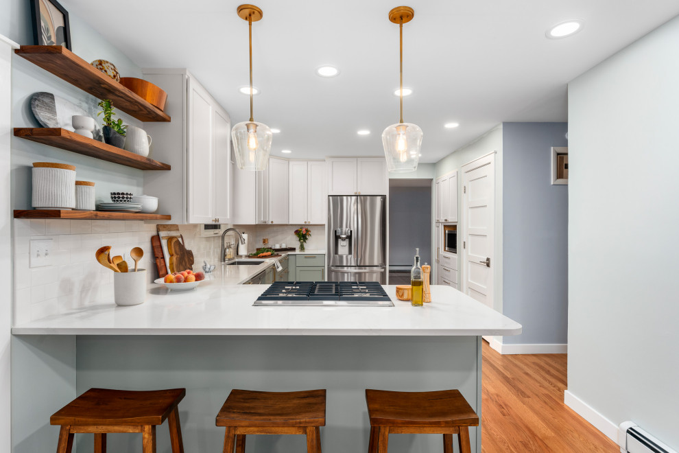 This is an example of a mid-sized transitional u-shaped kitchen in Denver with an undermount sink, shaker cabinets, green cabinets, quartz benchtops, white splashback, subway tile splashback, stainless steel appliances, medium hardwood floors, no island, brown floor and white benchtop.
