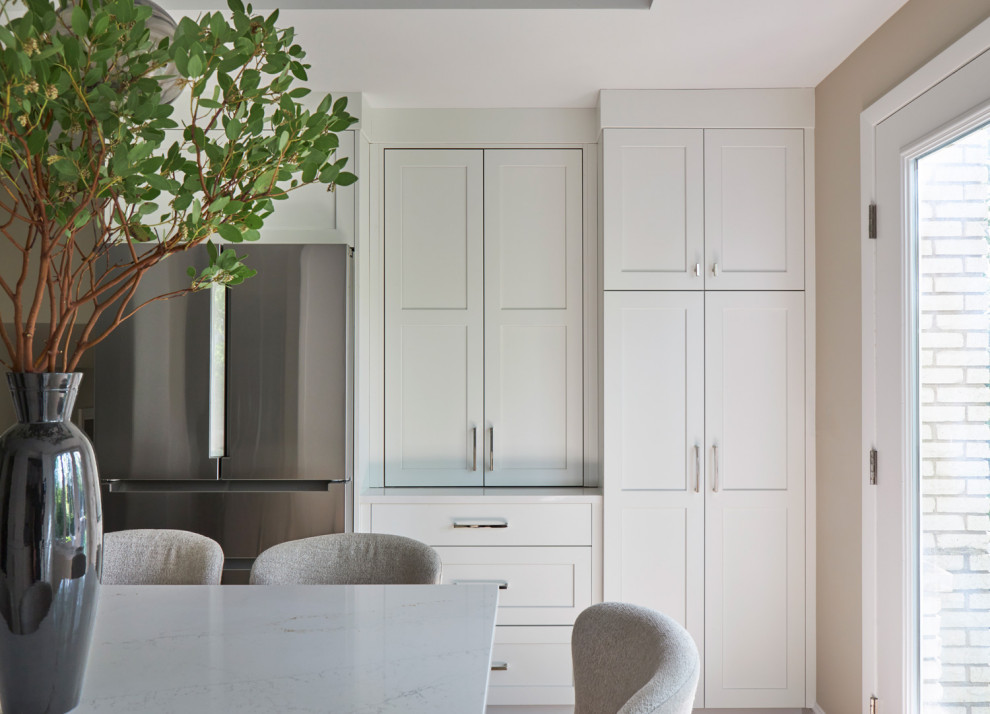 Large transitional u-shaped light wood floor, brown floor and coffered ceiling eat-in kitchen photo in Chicago with a farmhouse sink, shaker cabinets, white cabinets, quartz countertops, white backsplash, subway tile backsplash, stainless steel appliances, an island and multicolored countertops