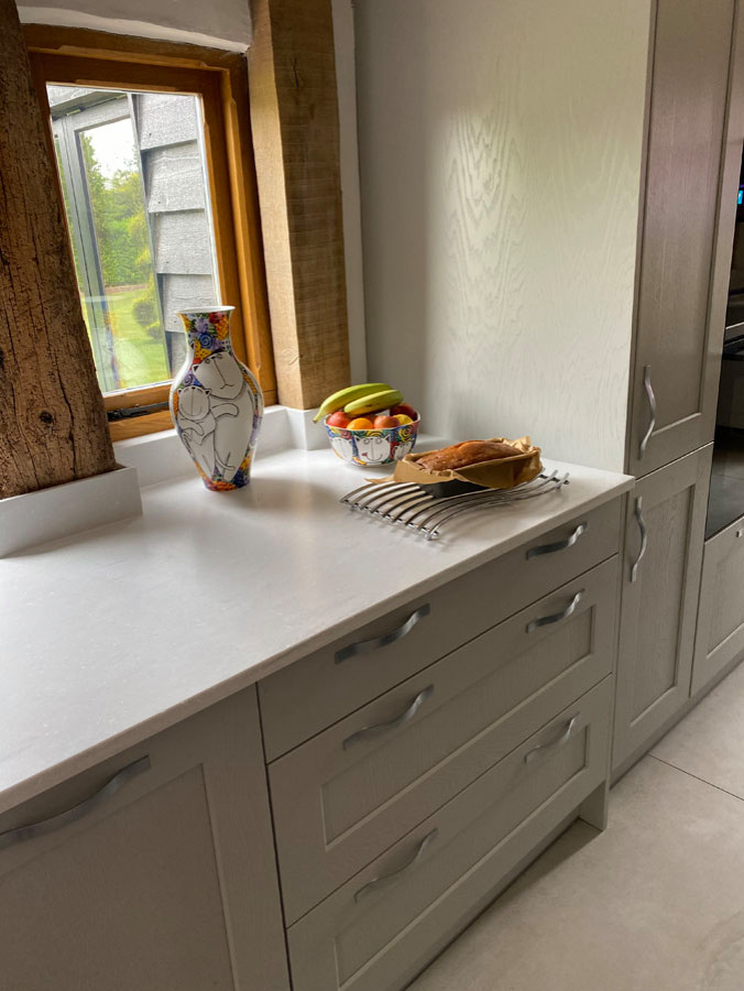 Photo of a large country l-shaped open plan kitchen in Essex with an integrated sink, shaker cabinets, grey cabinets, quartz benchtops, white splashback, black appliances, ceramic floors, with island, white floor and white benchtop.