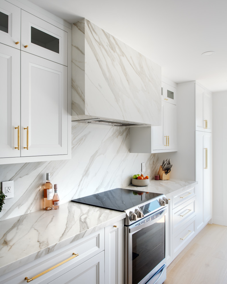 Example of a mid-sized transitional galley light wood floor and beige floor open concept kitchen design in Ottawa with an undermount sink, recessed-panel cabinets, white cabinets, quartz countertops, white backsplash, porcelain backsplash, stainless steel appliances, an island and white countertops
