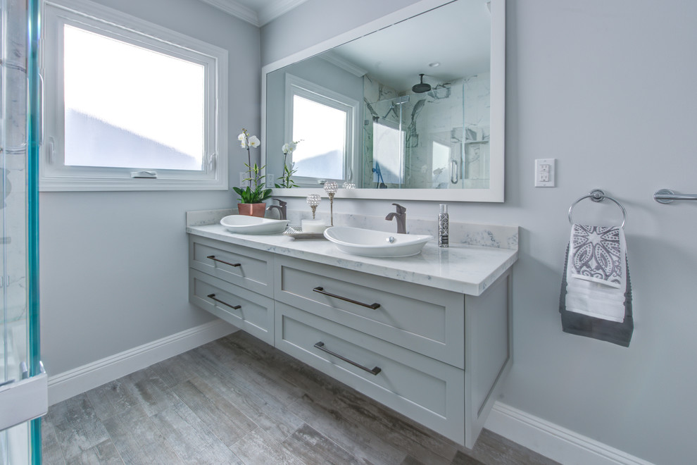 This is an example of a mid-sized transitional master bathroom in San Francisco with flat-panel cabinets, grey cabinets, an alcove tub, a shower/bathtub combo, a one-piece toilet, gray tile, porcelain tile, grey walls, porcelain floors, a vessel sink, engineered quartz benchtops, grey floor and a hinged shower door.