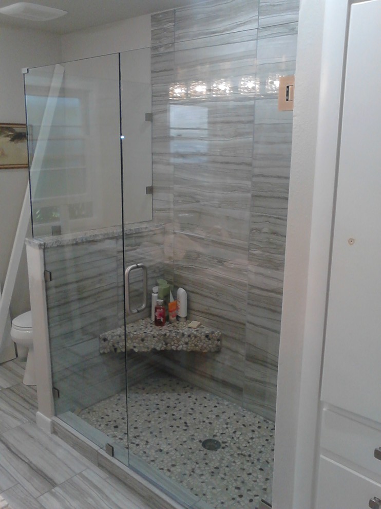 Corner shower - mid-sized transitional 3/4 gray tile and porcelain tile porcelain tile and gray floor corner shower idea with a one-piece toilet, beige walls and a hinged shower door