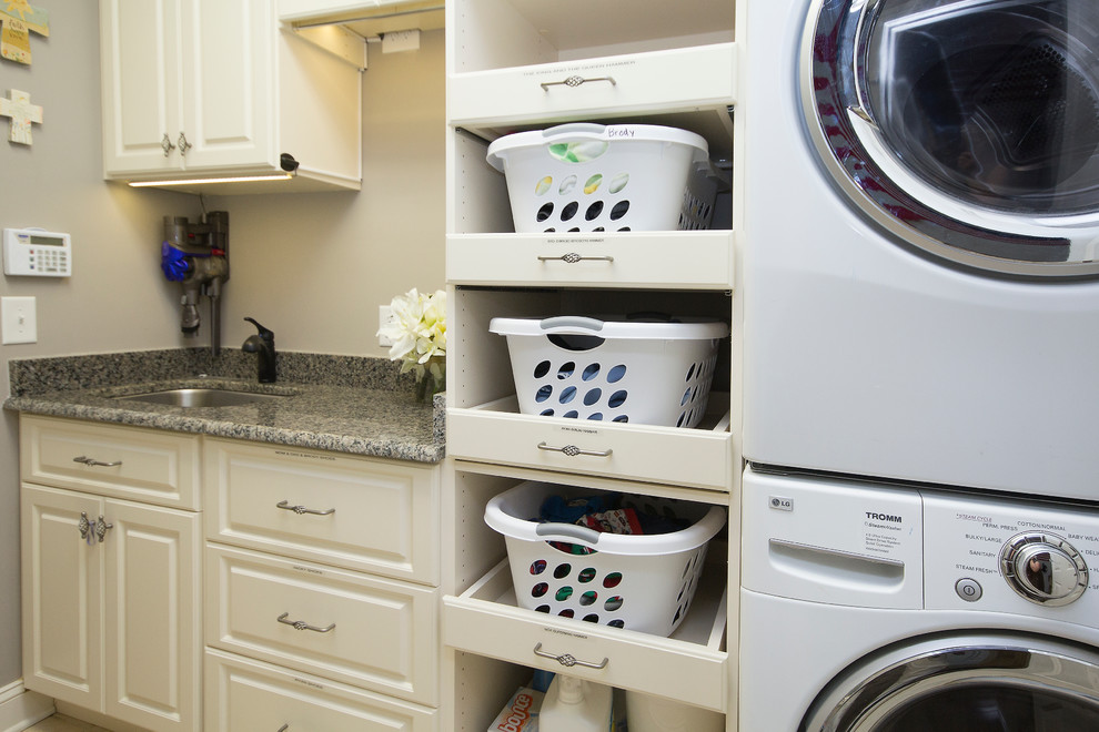 Photo of a mid-sized traditional dedicated laundry room in Raleigh with raised-panel cabinets, white cabinets, granite benchtops, beige walls, porcelain floors, a stacked washer and dryer, beige floor and an undermount sink.
