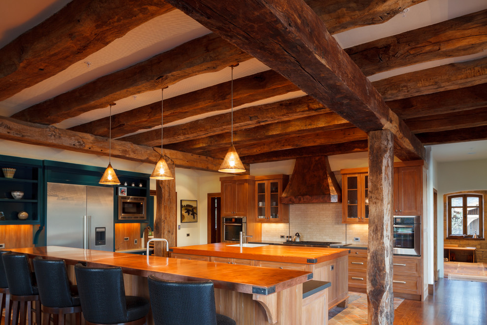 Large mountain style l-shaped medium tone wood floor and brown floor eat-in kitchen photo with a farmhouse sink, shaker cabinets, medium tone wood cabinets, soapstone countertops, beige backsplash, stone tile backsplash, stainless steel appliances and two islands