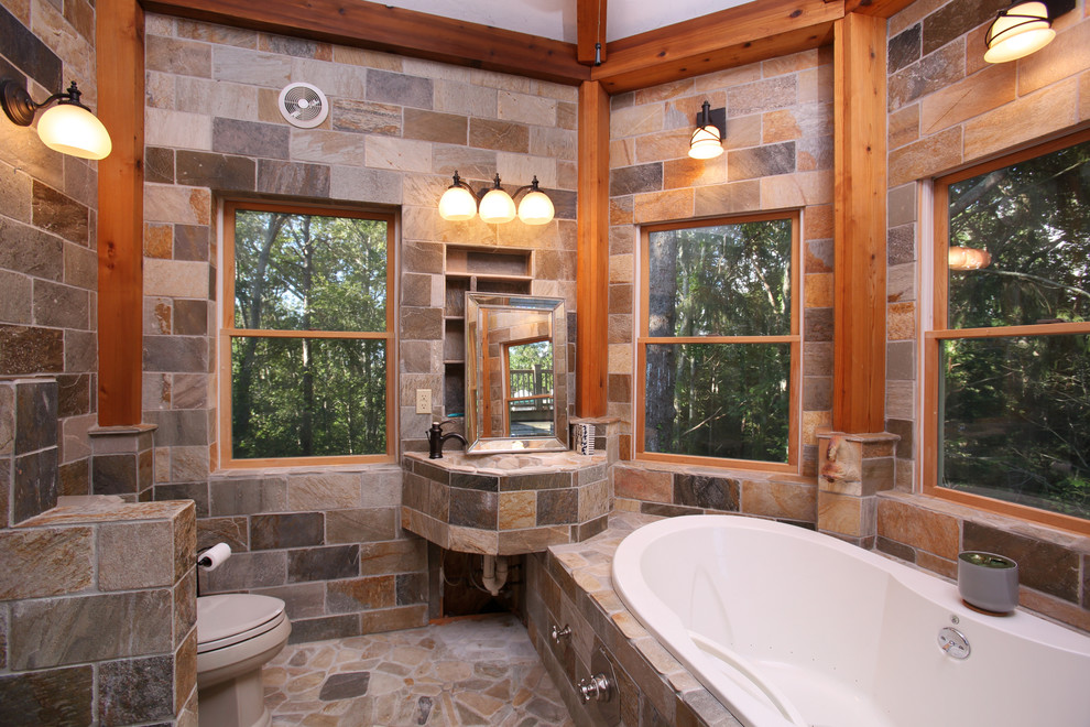 Country bathroom in Boston with a drop-in tub, a one-piece toilet, stone tile and an integrated sink.